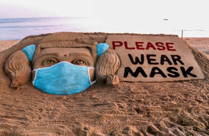 Sand artist Sudarsan Pattnaik creates a sand sculpture urging people to wear face masks for prevention against COVID-19, at Puri beach, Sunday, Jan. 9, 2022. (PTI Photo)