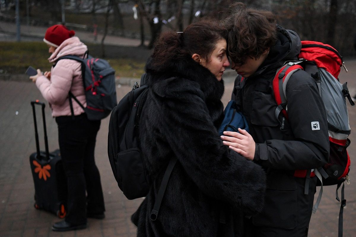 People hug as a woman with a suitcase uses her smartphone outside a metro station in Kyiv in the morning of February 24, 2022. Russian President Vladimir Putin announced a military operation in Ukraine on Thursday with explosions heard soon after across the country and its foreign minister warning a 