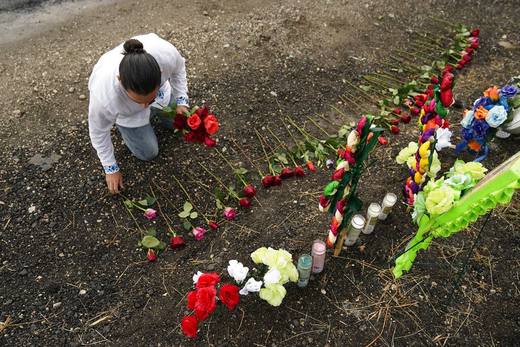Carlow Eduardo Espina places roses on a make-shift memorial at the site where officials found dozens of people dead in a semitrailer containing suspected migrants, Tuesday, June 28, 2022, in San Antonio. (AP Photo/Eric Gay)